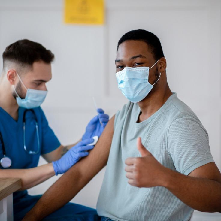 African american man in mask gesturing thumb up during coronavirus vacination